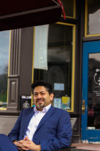 Felipe sitting and smiling with a building entrance as the background